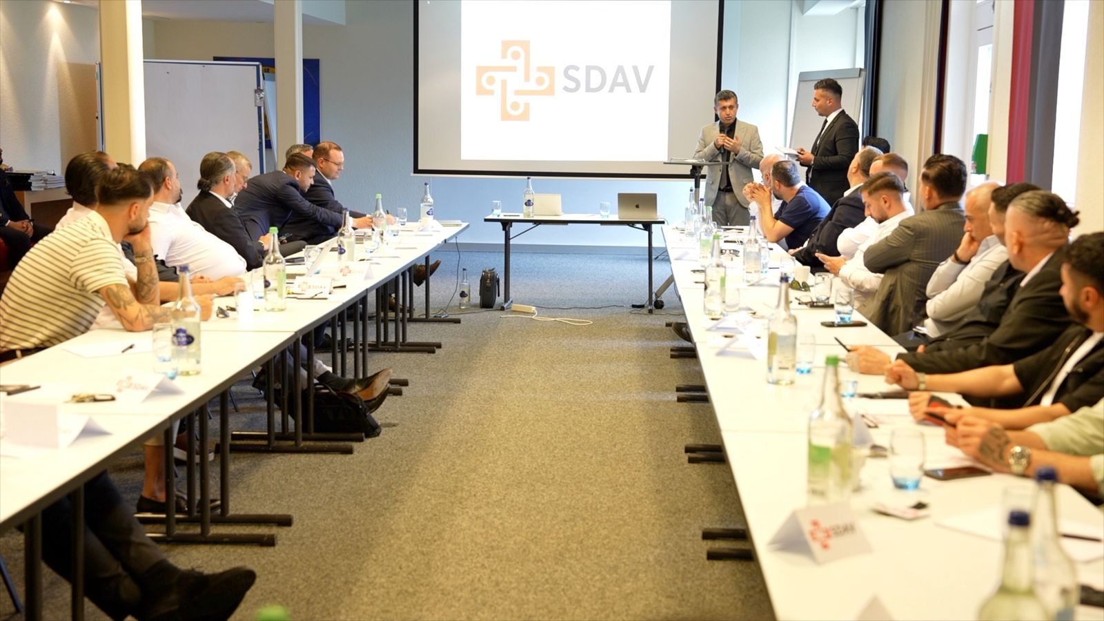Participants seated along a U-shaped table at the SDAV networking evening in Egerkingen; the SDAV logo is projected on the screen while two speakers address the room.