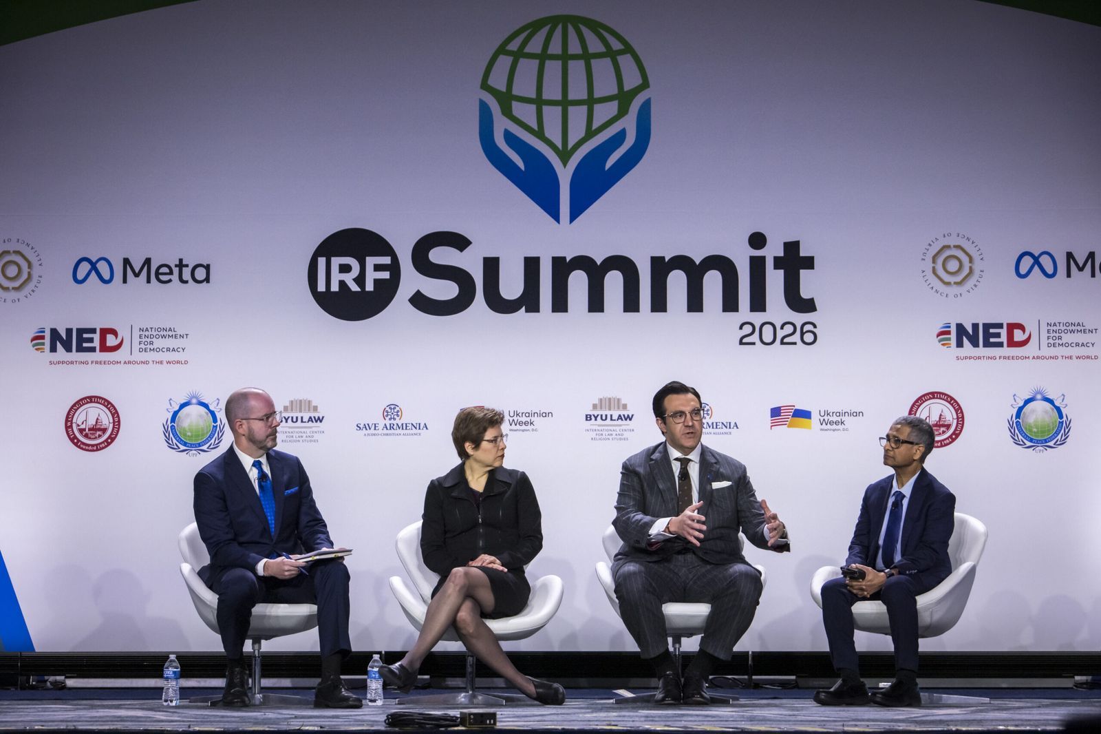 Four panellists seated in white armchairs on the main stage of the IRF Summit 2026, in front of the summit backdrop with partner logos.