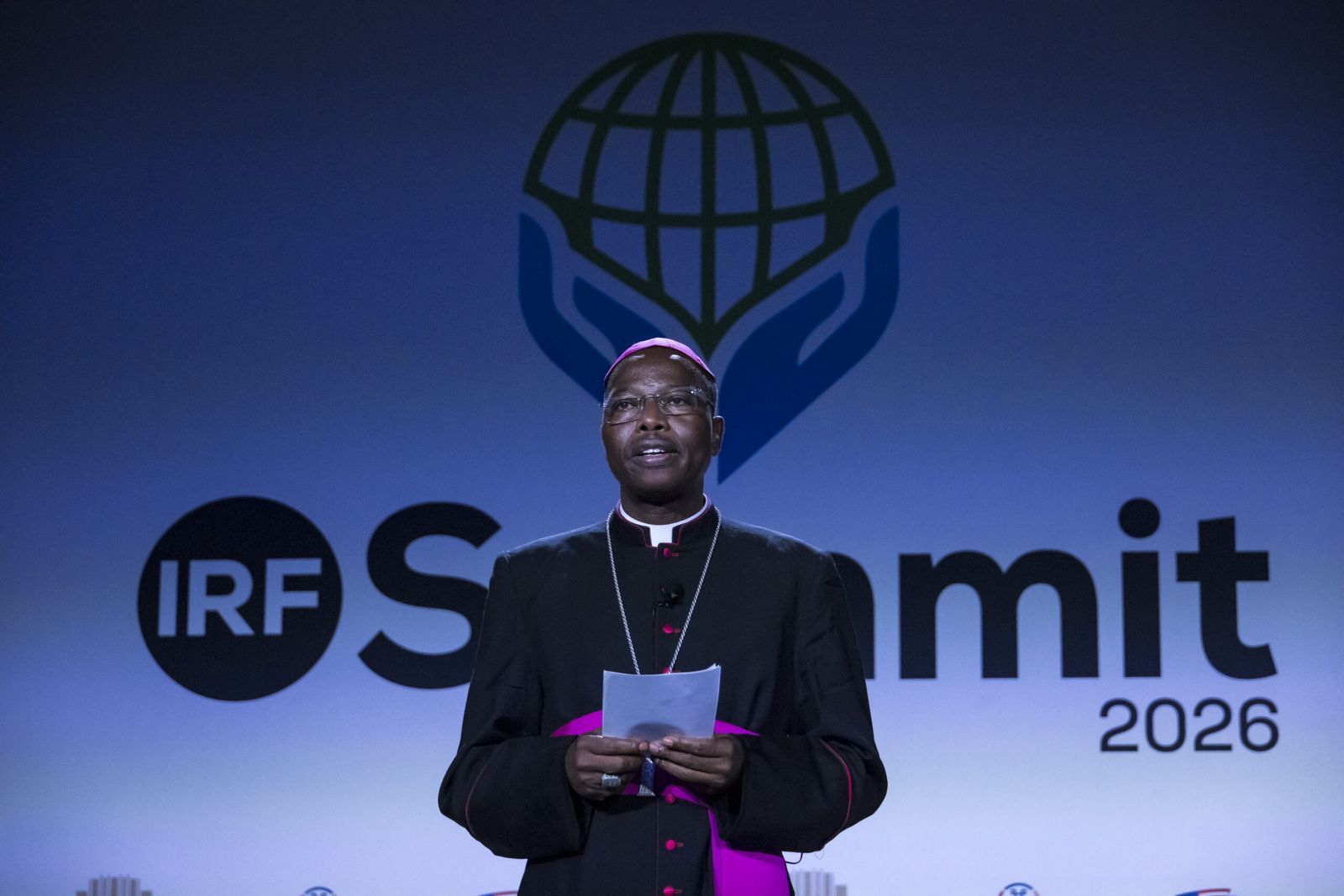 A speaker addresses the plenary from the main stage, in front of the IRF Summit 2026 logo.