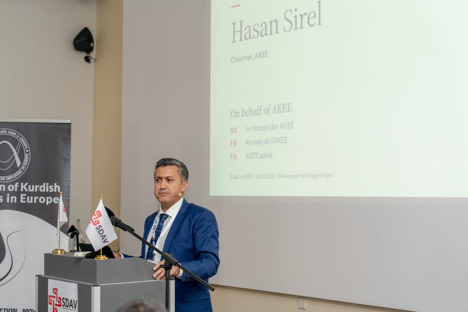 Hasan Sirel, chairman of AKEE, speaking at the lectern, his title slide on the screen.