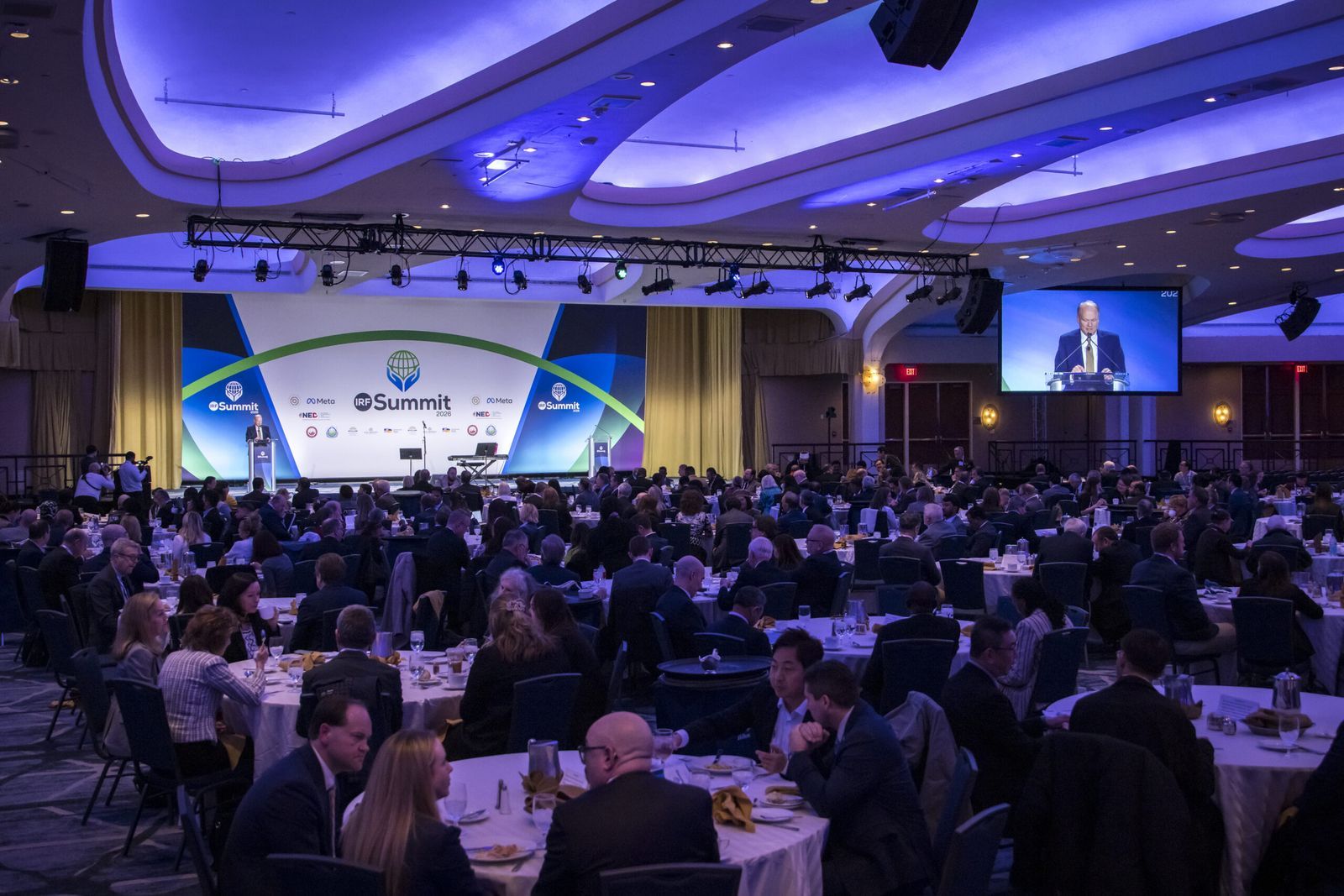 The plenary hall of the IRF Summit 2026 at the Washington Hilton: participants seated at round tables during a session, the stage and a large screen at the back.