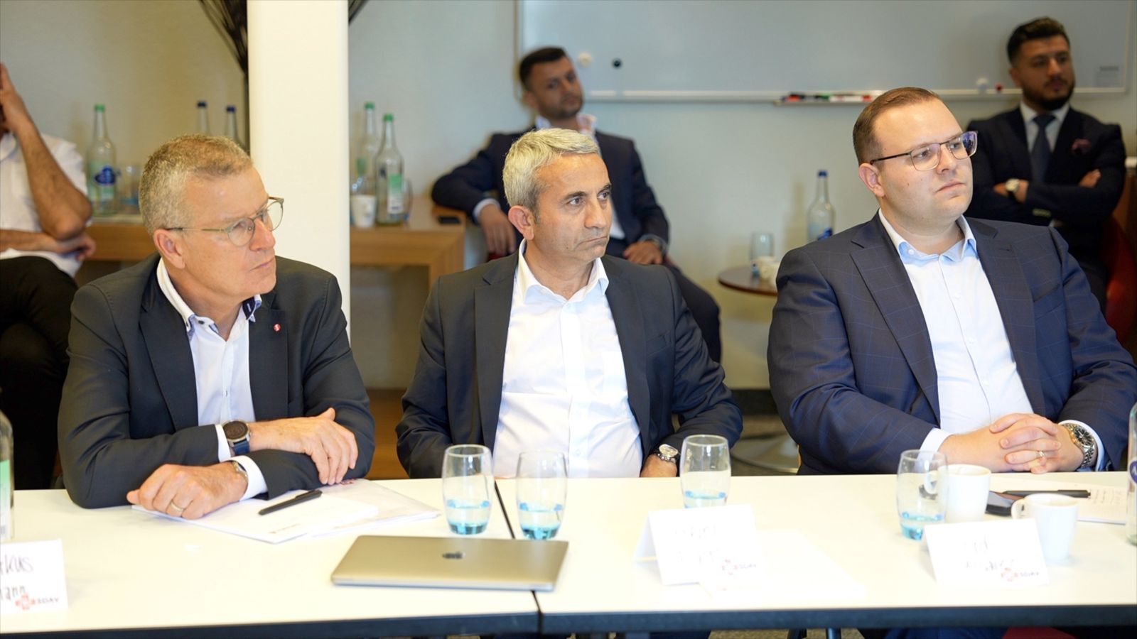 Three participants seated at the table during the talks, listening, with SDAV name cards in front of them.