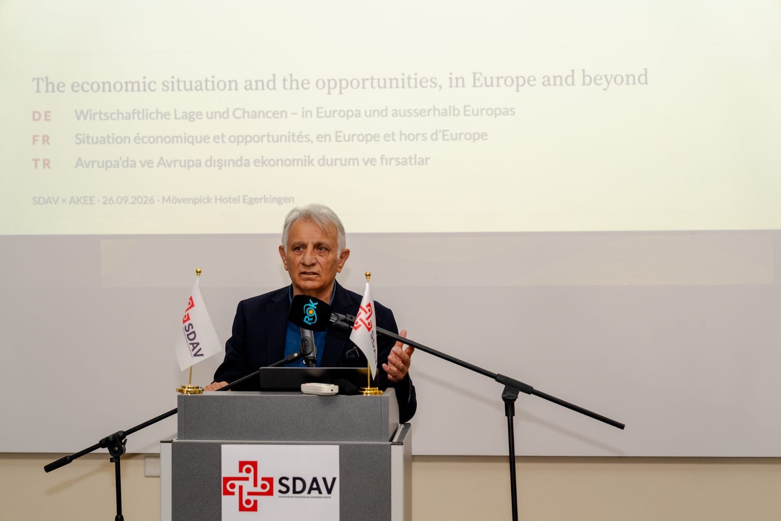 Erol Katırcıoğlu at the lectern; the slide gives the title of his talk on the economic situation in Europe and beyond.
