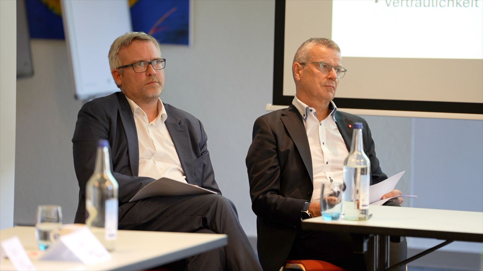 Two guests seated side by side, following a presentation with papers in hand.