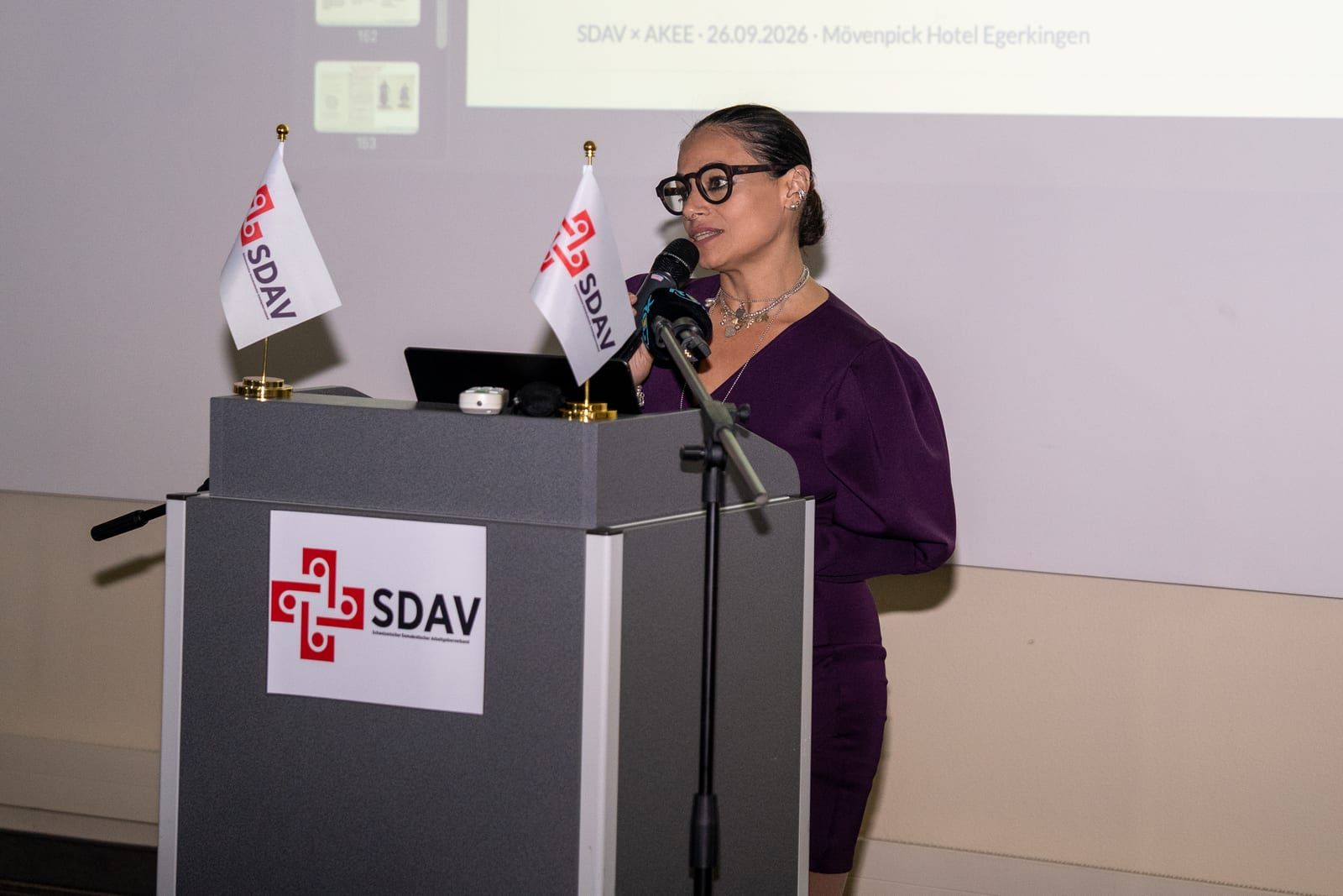 Nurgül Çokgezici at the lectern with a notebook in hand, the SDAV sign on the front of the lectern.