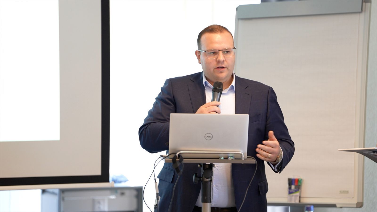 A speaker with a microphone at the laptop lectern, addressing the room.