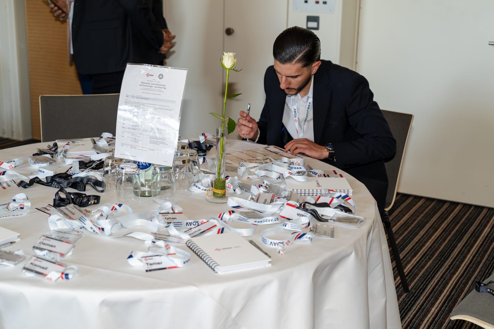 The registration table: SDAV lanyards and name badges laid out, a printed programme in a stand, a white rose in a vase.